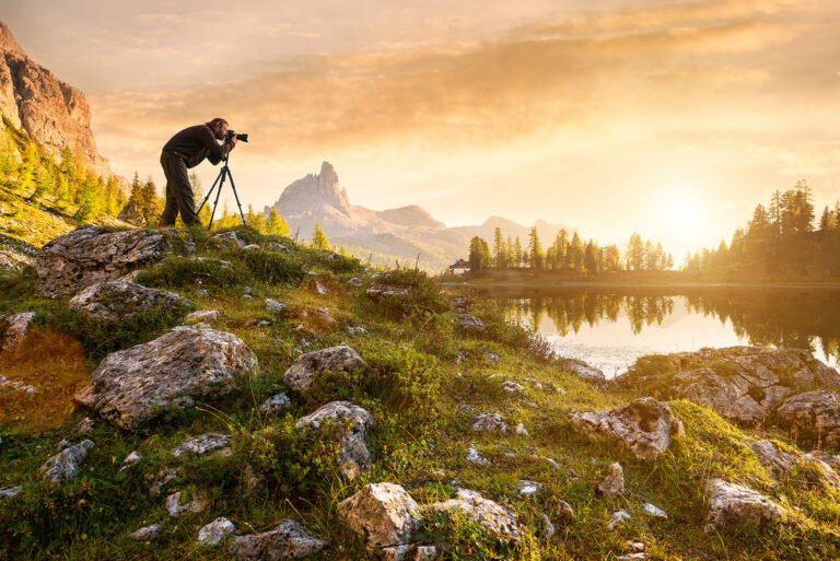 Fotógrafo con trípode fotografiando un paisaje de montaña y lago al atardecer